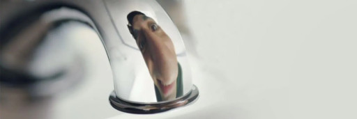 This image depicts the smiling reflection of a man's face in the spout of a tap. His face appears playfully distorted, exaggerating the size of his nose.