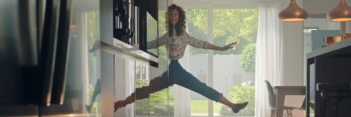 This image depicts a smiling young woman playing with her reflection in the shiny cabinets of her kitchen, it appears that she's suspended in mid-air.