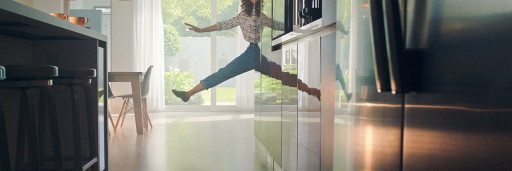 This image depicts a woman who jumps in her kitchen, she is smiling.