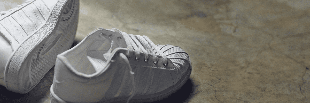 This image depicts a pair of bright white canvas trainers lying on the floor